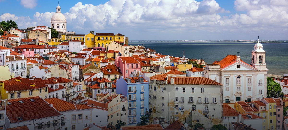 Вид на район Алфама в Лиссабоне: разноцветные дома, красные крыши и океан на фоне